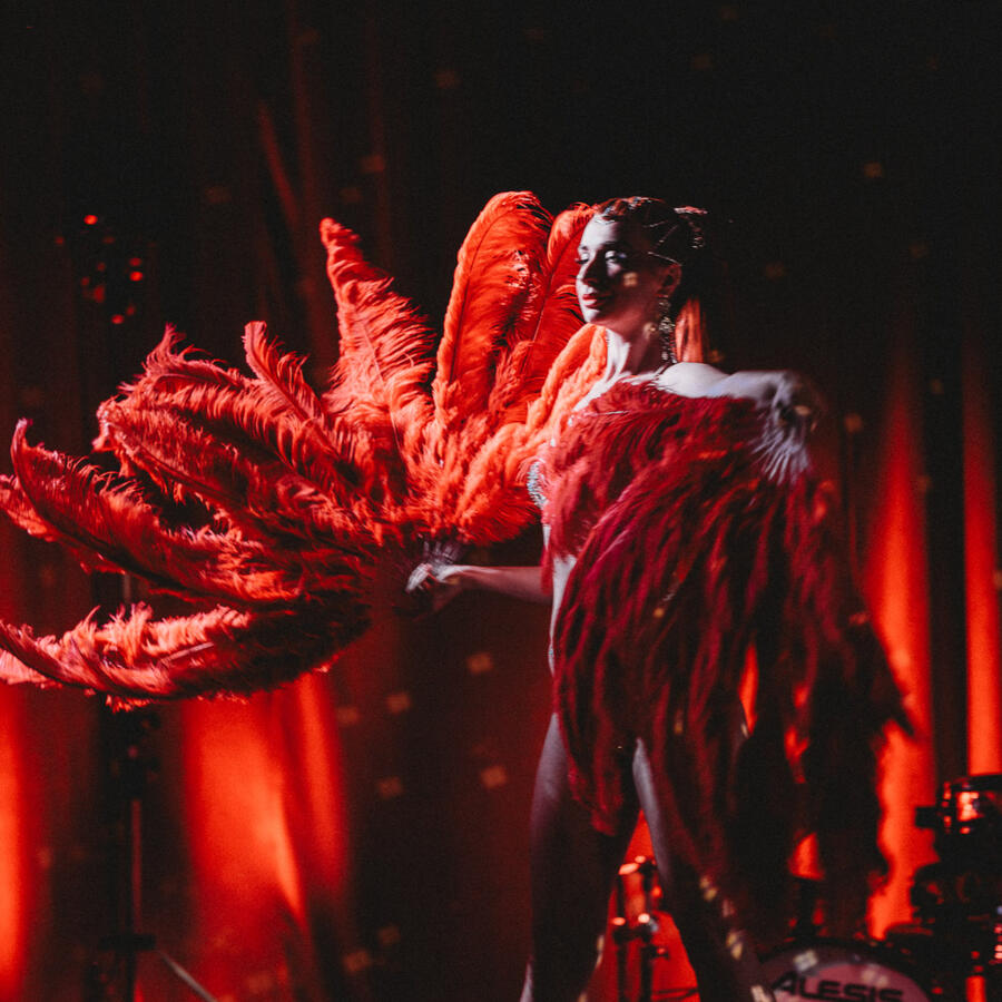 Untitled Catrice Cat, lektorka a tanečnica, v dramatickej póze s veľkými perovými vejármi na burlesque show Hall of Tease